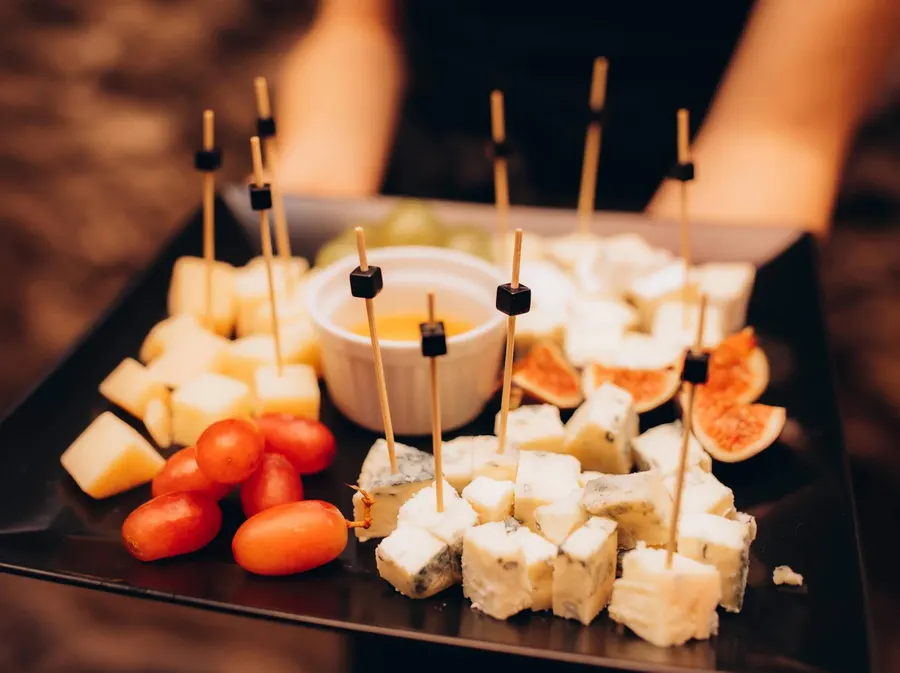 A platter of cheese cubes, cherry tomatoes, figs and honey dip served on cocktail skewers