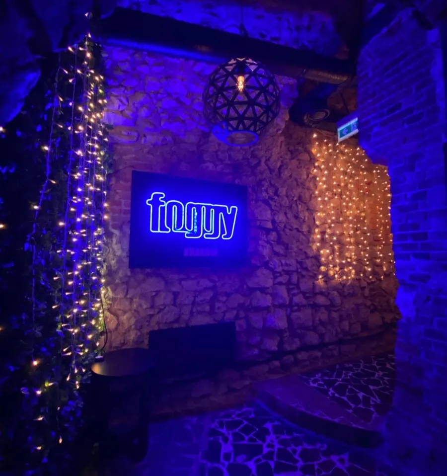 Glowing blue Foggy Krakow neon sign on a stone wall framed by warm fairy lights