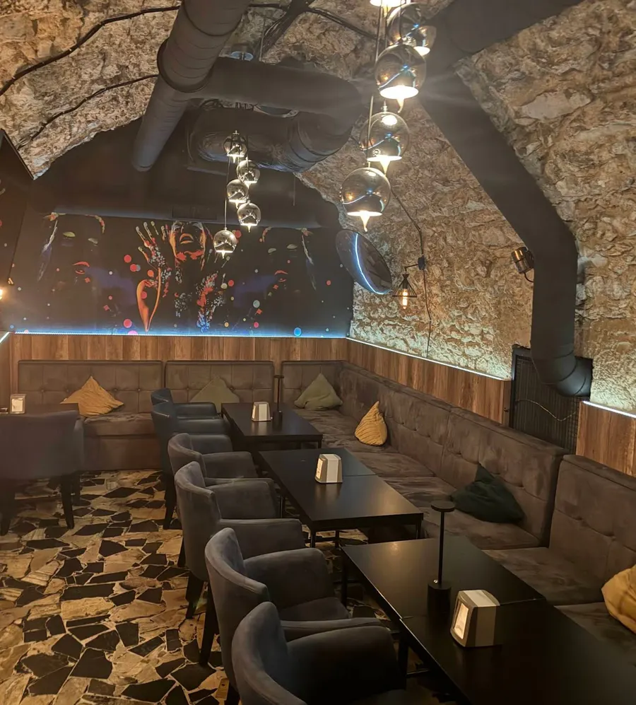 Vaulted stone lounge interior with velvet banquettes, dark tables and a colorful mural